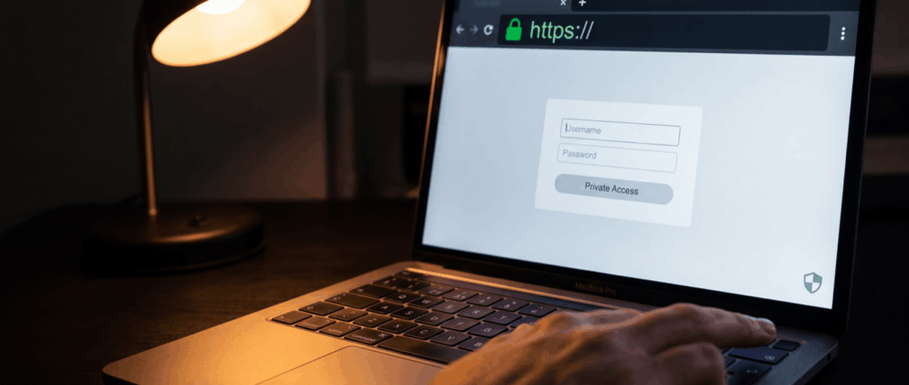 Laptop screen displaying a login page with fields for "Username" and "Password" under "Private Access," illuminated by a desk lamp.