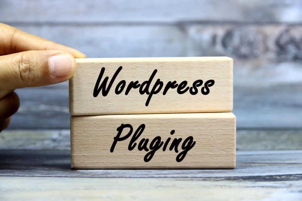 Hand holding a wooden block with "Wordpress" stacked on another block labeled "Pluging" against a wooden background.